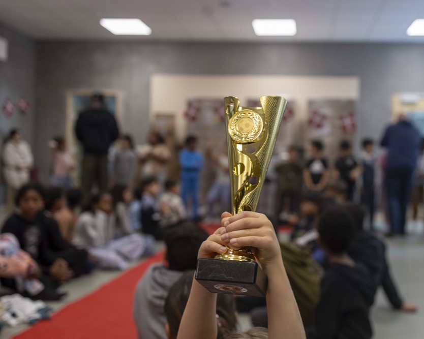 To hænder holder guldfarvet pokal op i luftet