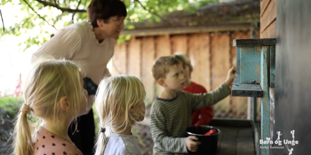 Fire børn og en voksen leger ved et legehus