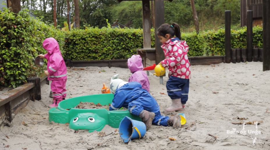 Børn i regntøj leger i sandkassen