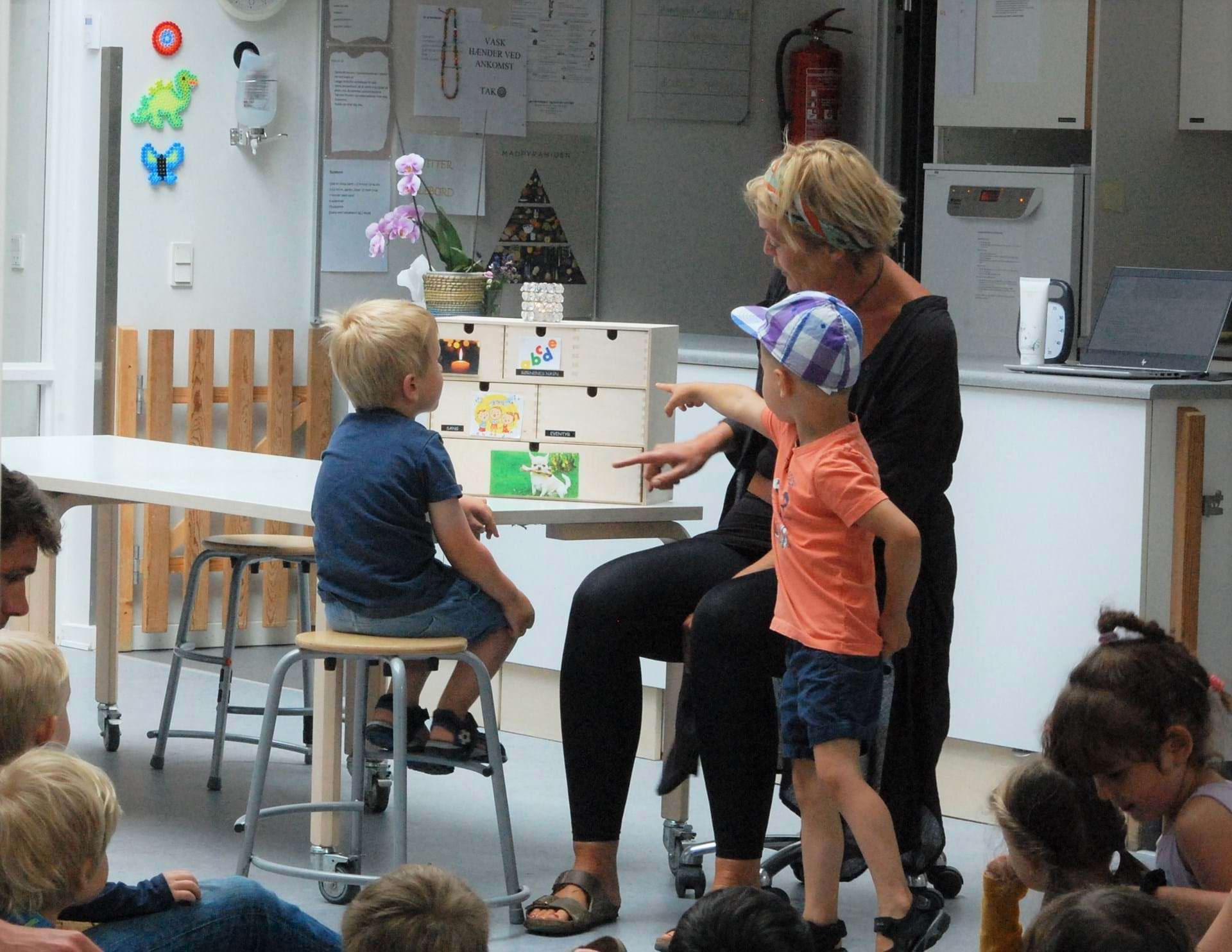 Børn og pædagog peger på skuffer