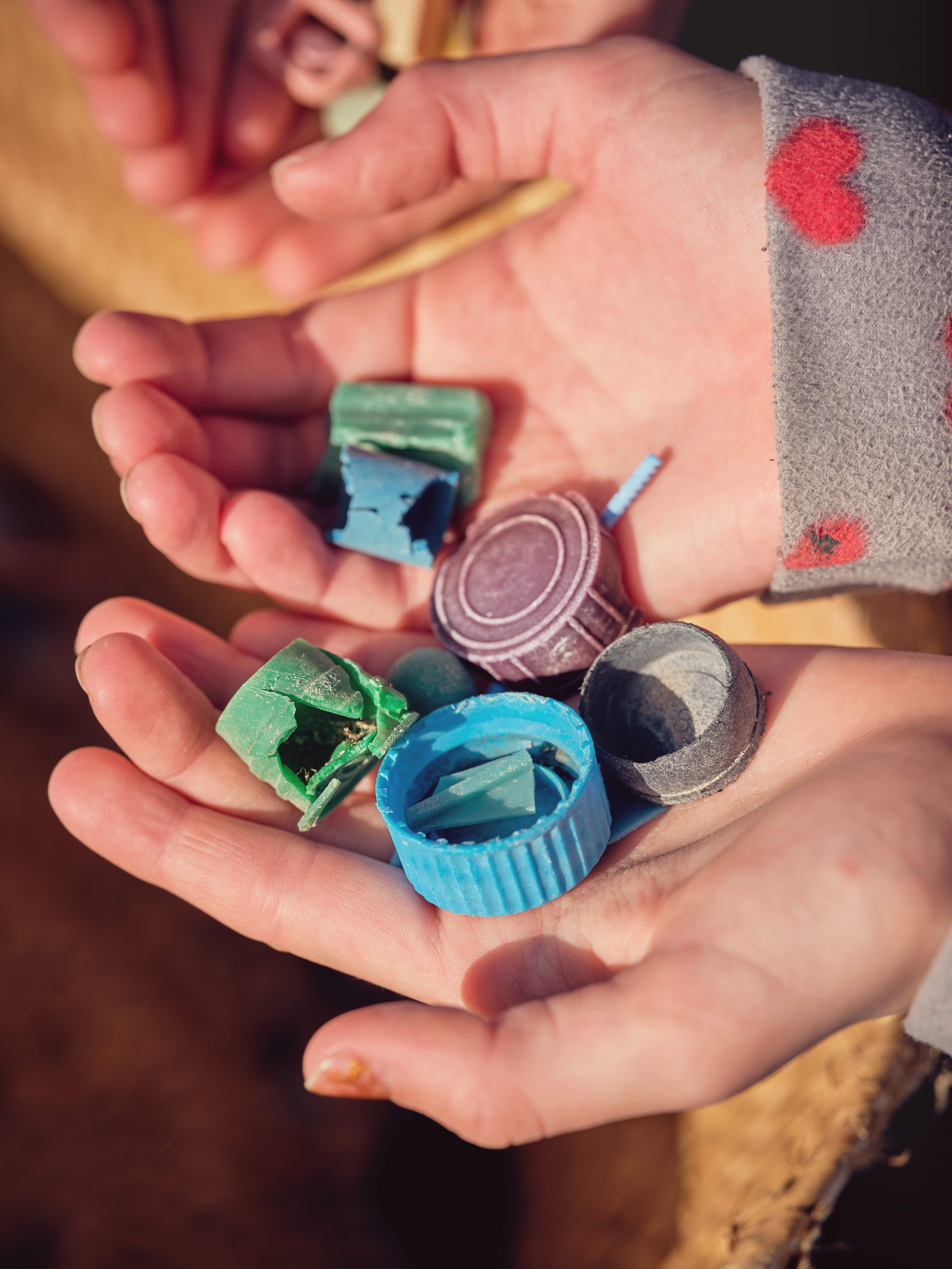 Et barns hænder fyldt med gamle plasticlåg