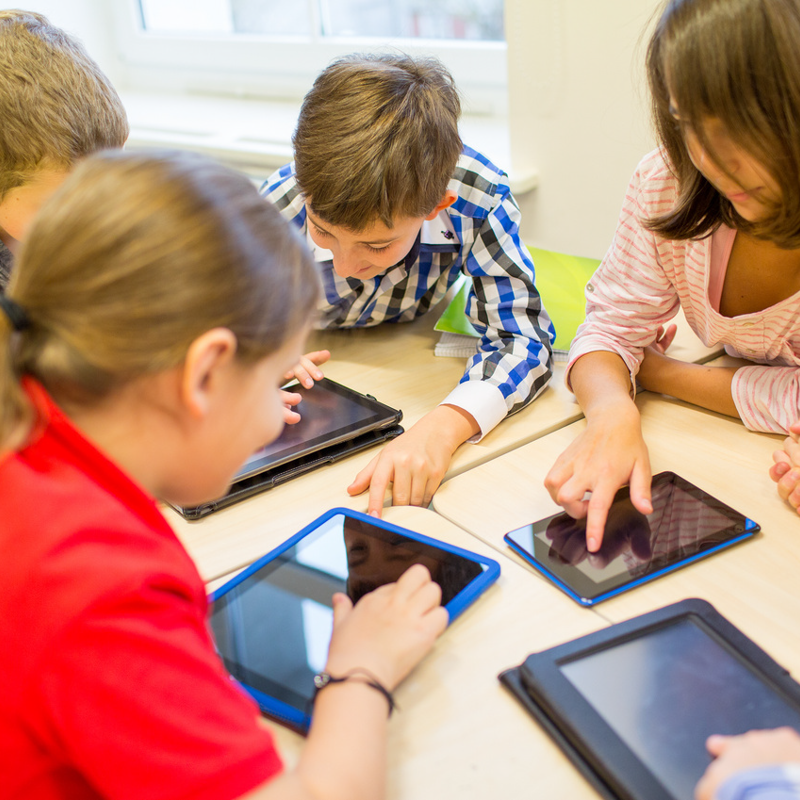 Skolebørn med tablets ved et bord i skolen