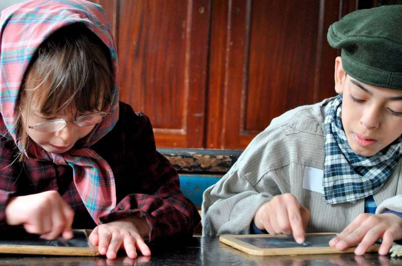 To børn i en gammeldags skole med tavler og kridt