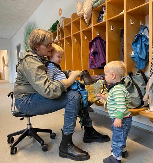 Voksen med to børn der tager tøj på i legestuen