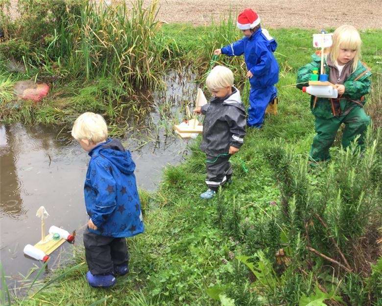 Fire børn med små tømmerflåder ved vandløb 